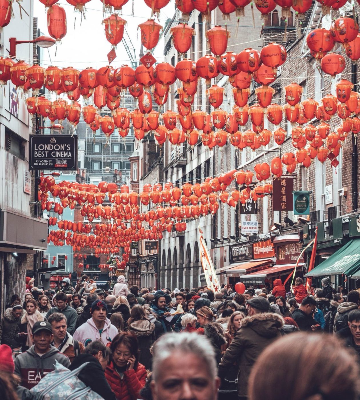 A street in London's Chinatown during a festival: strings of red lanterns above a dense crowd of people of many ages and backgrounds